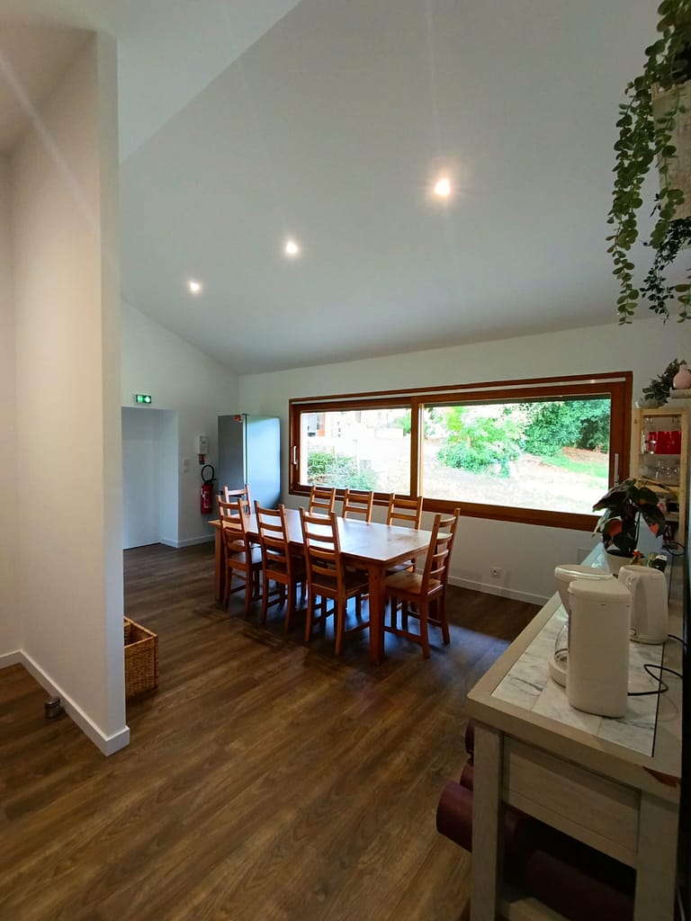 Cette photo montre une salle de réception lumineuse et conviviale, idéale pour les évènements d'entreprise, les séminaires, les ateliers bien-être ou le coworking. L'espace comprend un vidéoprojecteur, de grandes tables modulables, des chaises confortables, ainsi qu'un coin détente avec canapés. Une cuisine entièrement équipée permet d'organiser des pauses cafés ou des repas sur place. L'ambiance chaleureuse et professionnelle crée un cadre propice à la collaboration et à la créativité